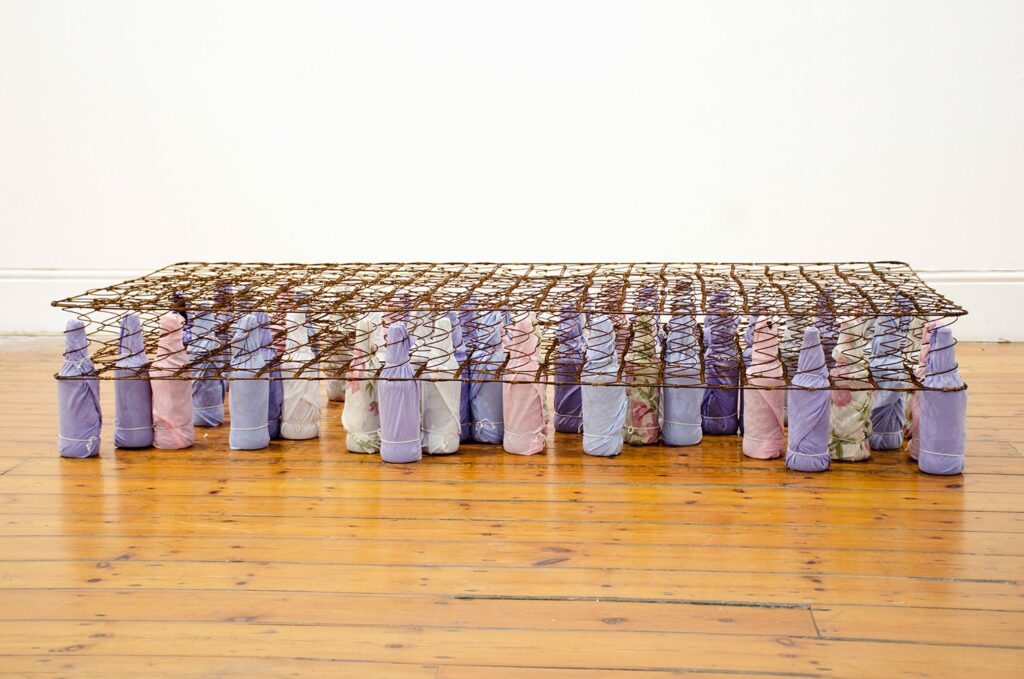 Lungiswa Gqunta , Let Me Ease The Pain, 2016. Bed spring, beer bottles, bed linen, string 30 x 190 x 90 cm. (11,8 x 74,8 x 35,4 inches). Courtesy the artist.