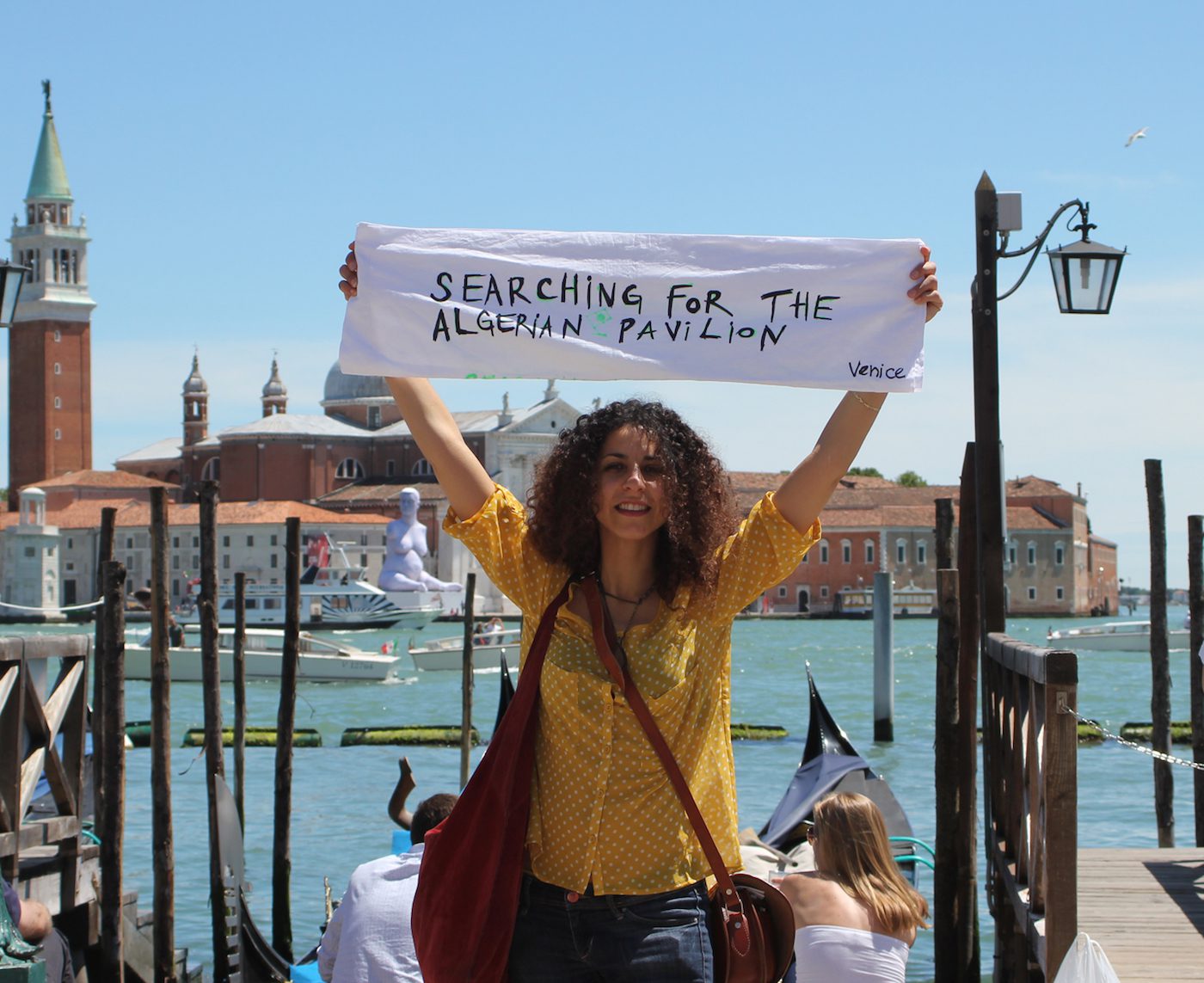 Amina Zoubir, Searching for the Algerian Pavilion, photograph of the performance made in June 3rd 2013 during The Venice Biennale, behind sculpture of Marc Quinn on the island San Giorgio Maggiore, 120x80 cm, 2013. © Amina ZOUBIR ADAGP Paris
